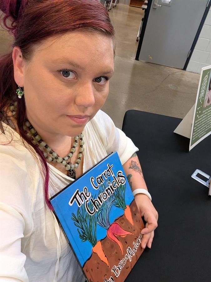 An adult holding a blue illustrated book titled The Carrot Chronicles