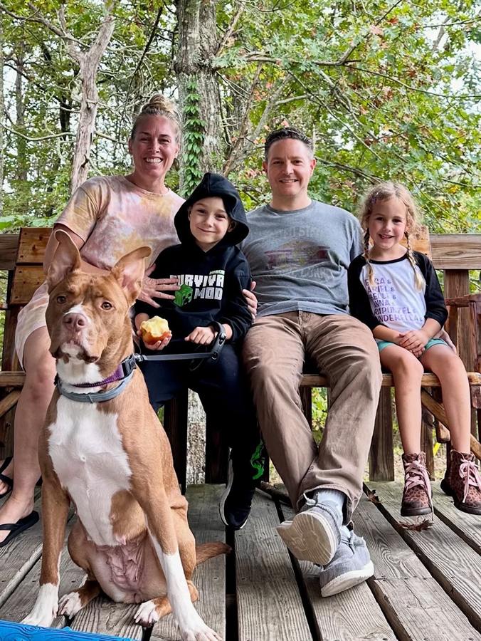 Two adults and two children sitting outdoors with a dog