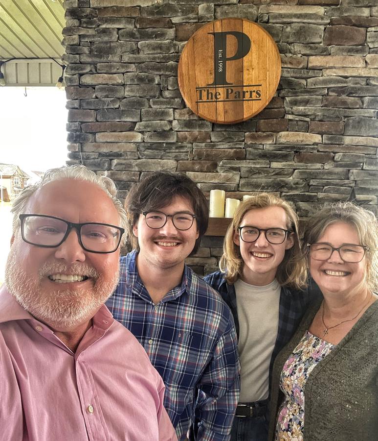 Four adults posing beneath a round wooden sign reading The Parrs