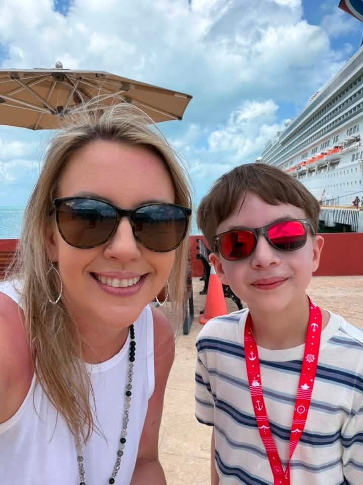 An adult and a child wearing sunglasses near a cruise ship