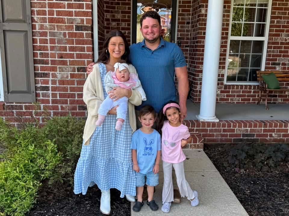 Two adults and three children standing together outside a brick home