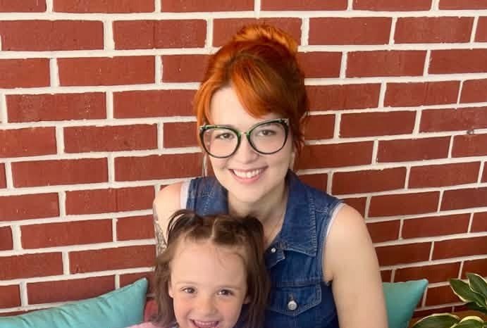 An adult and child smiling in front of a brick wall